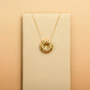 Gold necklace with a donut-shaped pendant on a beige card against a beige background
