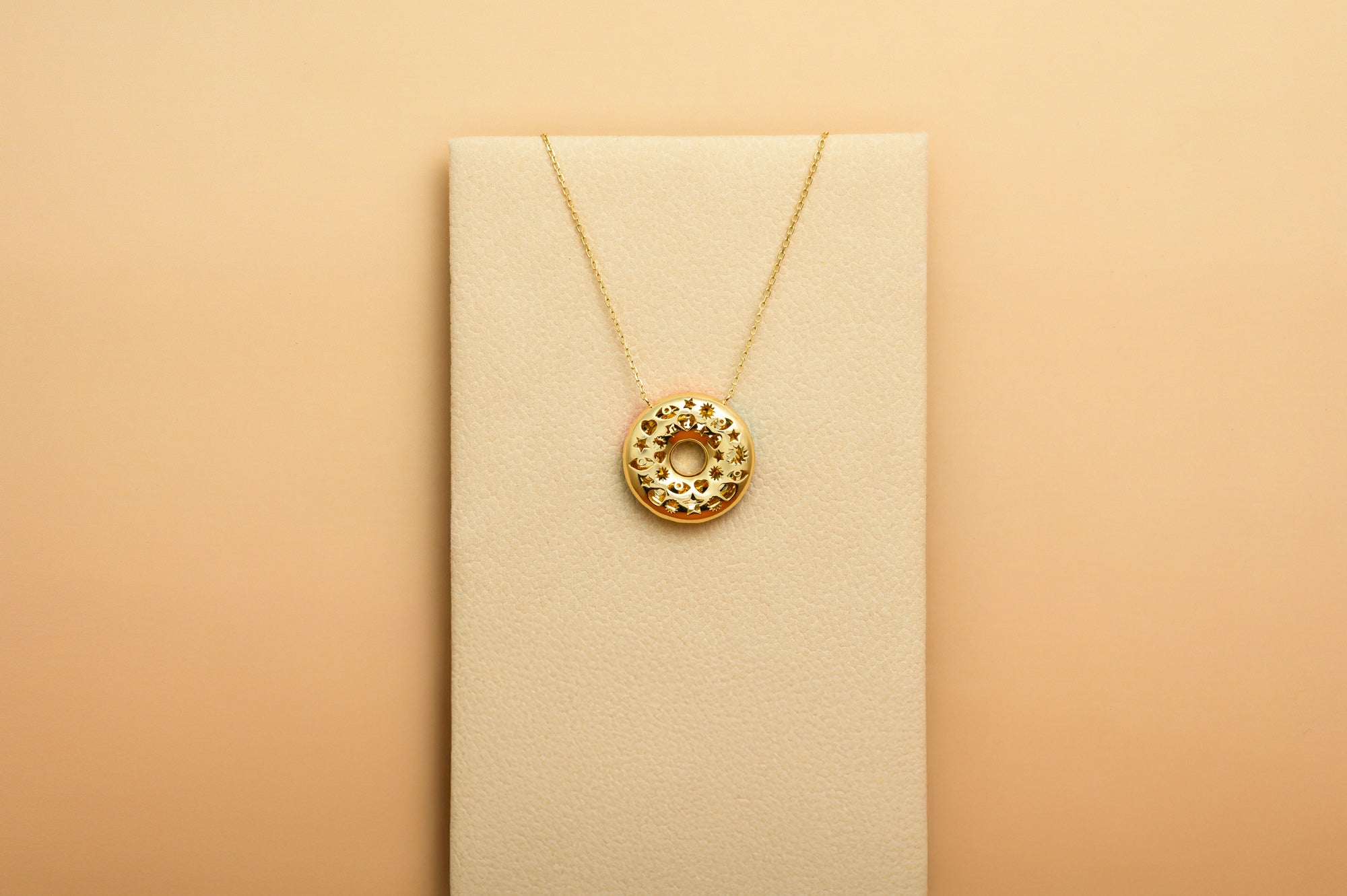 Gold necklace with a donut-shaped pendant on a beige card against a beige background